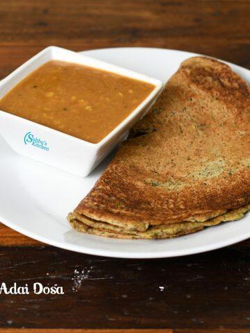 Close-up of a golden-brown, protein-rich adai dosa on an iron tawa, garnished with fresh curry leaves and served alongside chutney and sambar.