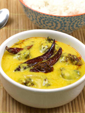 A delicious bowl of Kadhi Pakora, featuring golden, crispy pakoras served in a creamy, tangy yogurt gravy, garnished with fresh cilantro and a tempering of mustard seeds and curry leaves.